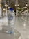 A clear plastic water bottle with a blue label and cap is set on a glossy marble surface. In the background, the interior of a grand building features tall, ornate columns with intricate patterns and soft lighting from gold and white fixtures.