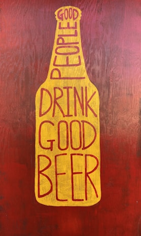 A graphic stylized as a beer bottle with the text 'Good People Drink Good Beer' written in bold, uppercase letters. The design features a mustard yellow bottle shape against a textured, dark reddish-brown background.