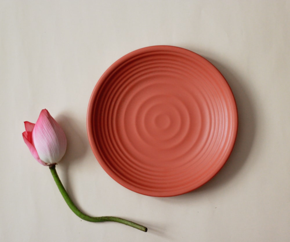 둥근 빨간 둥근 접시 옆에 분홍색과 흰색 꽃 봉오리