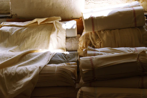 Close-up of industrial fabric rolls stacked neatly in a warehouse with soft natural light highlighting their textures.
