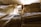 Several large bundles of fabric or textile are neatly stacked in a dimly lit room. The fabrics are rolled and tied, showcasing a variety of textures, with some striped patterns visible. Sunlight partially illuminates the scene from above, casting soft shadows.