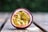 Half of a passion fruit rests on a wooden surface, showcasing its vibrant yellow pulp and dark seeds. The outer skin is a deep purple color, providing a contrast against the bright interior. The background is blurred, with a greenish tone.
