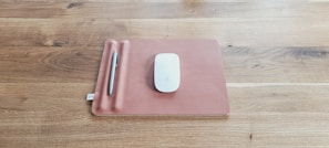A leather mouse pad and matching coaster set placed beside a laptop in a bright office space.