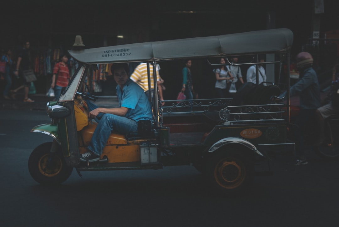 man in blue denim jacket sitting on black and white auto rickshaw during night time