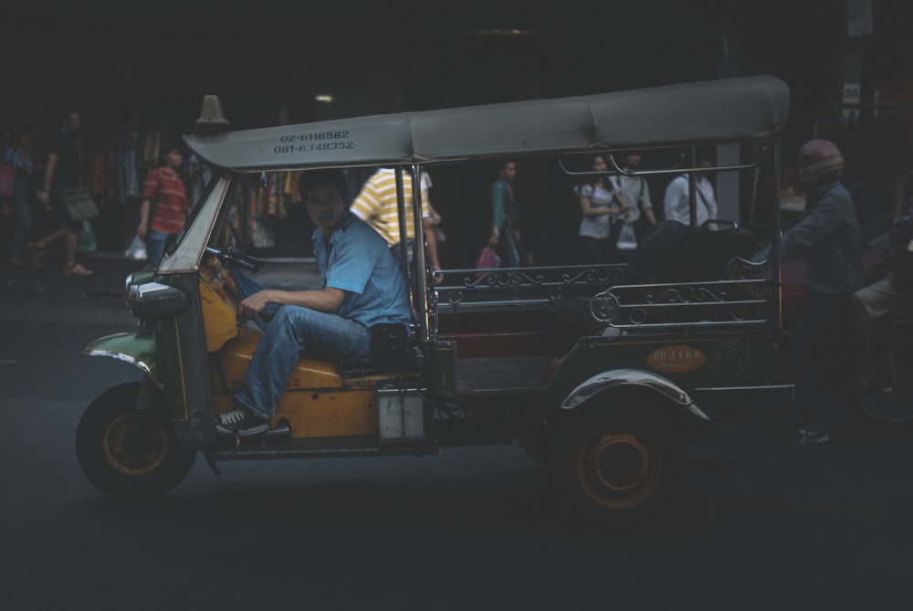 man in blue denim jacket sitting on black and white auto rickshaw during night time