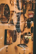 A wall filled with various styles of clocks, ranging from modern to classic designs. The lighting gives a warm, vintage ambiance. Some clocks are round, others are square, and there is a visible price tag indicating a sale. The foreground shows glass reflections.