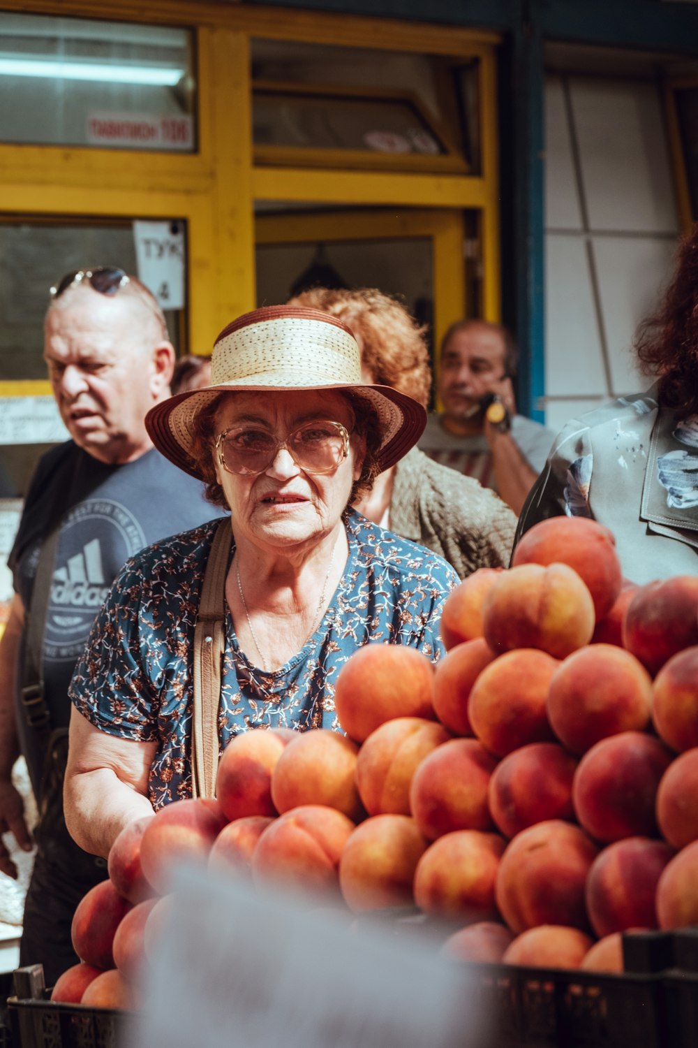 woman in brown hat and white and black floral shirt holding red apple fruit