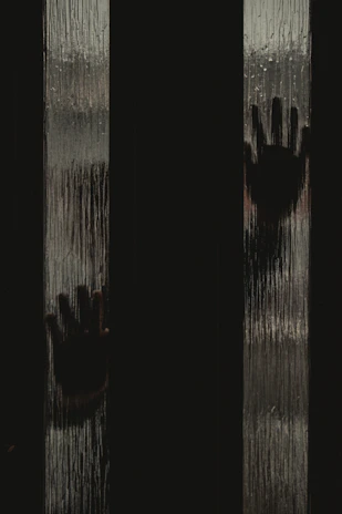 A mysterious hand pressed against a foggy glass pane with dim golden light filtering through.