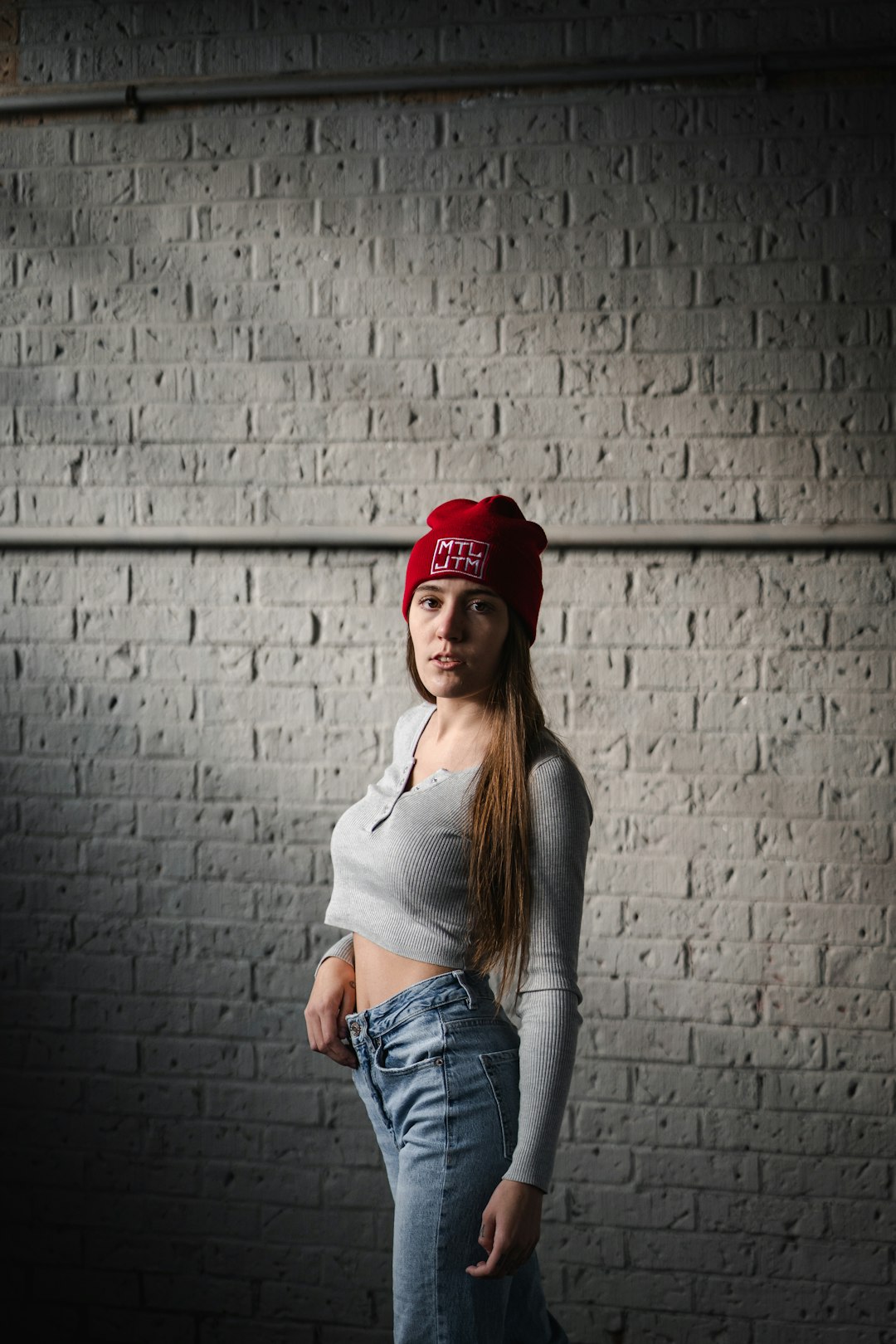 woman in white tank top and red knit cap leaning on grey brick wall