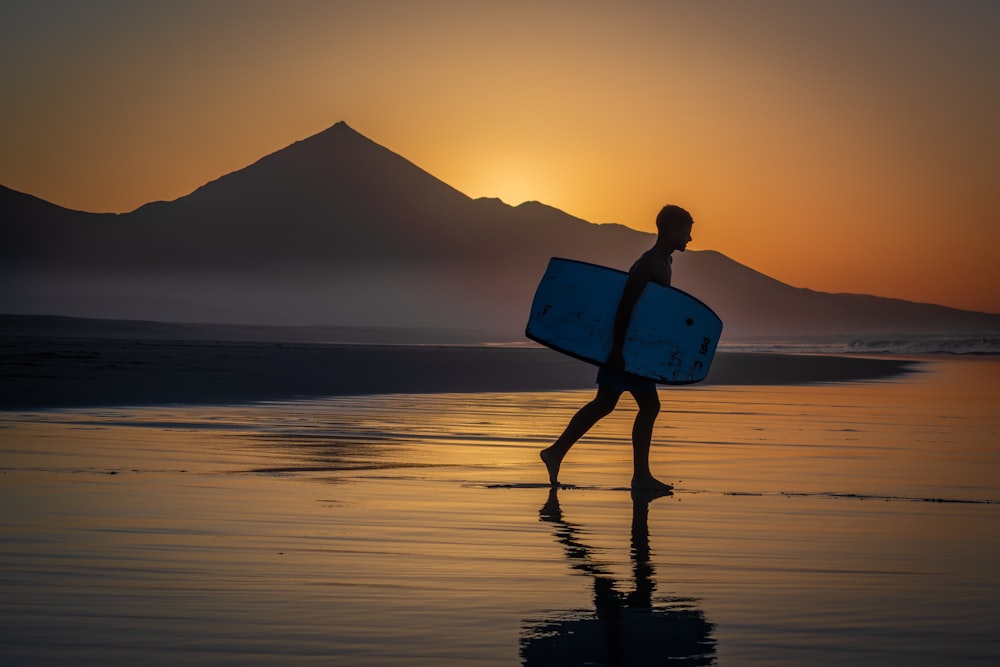man holding red surfboard walking on beach during sunset