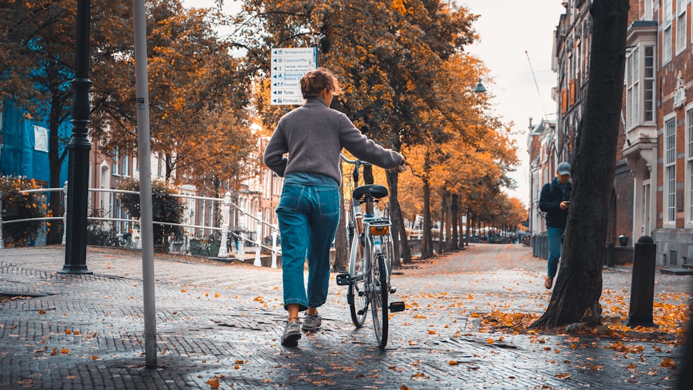 man in gray hoodie and blue denim jeans standing on gray concrete pavement near brown trees