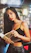 A warm, close-up portrait of a smiling woman holding a copy of 'Memoir of Pinky Monroe' against a cozy bookshelf backdrop.