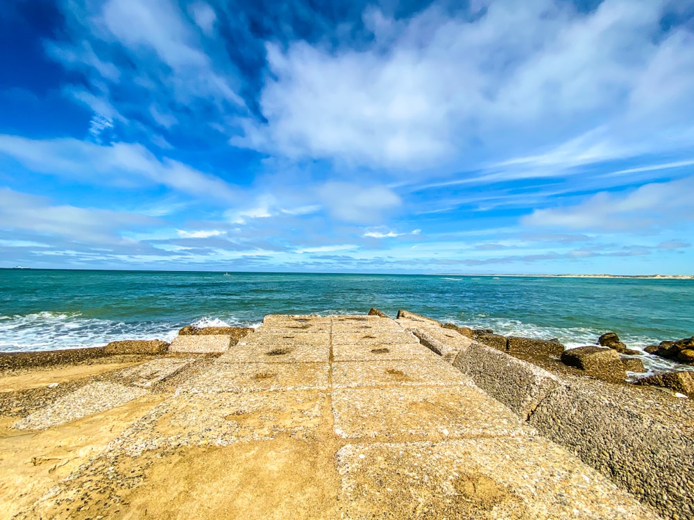 brown concrete pathway near sea under blue sky during daytime