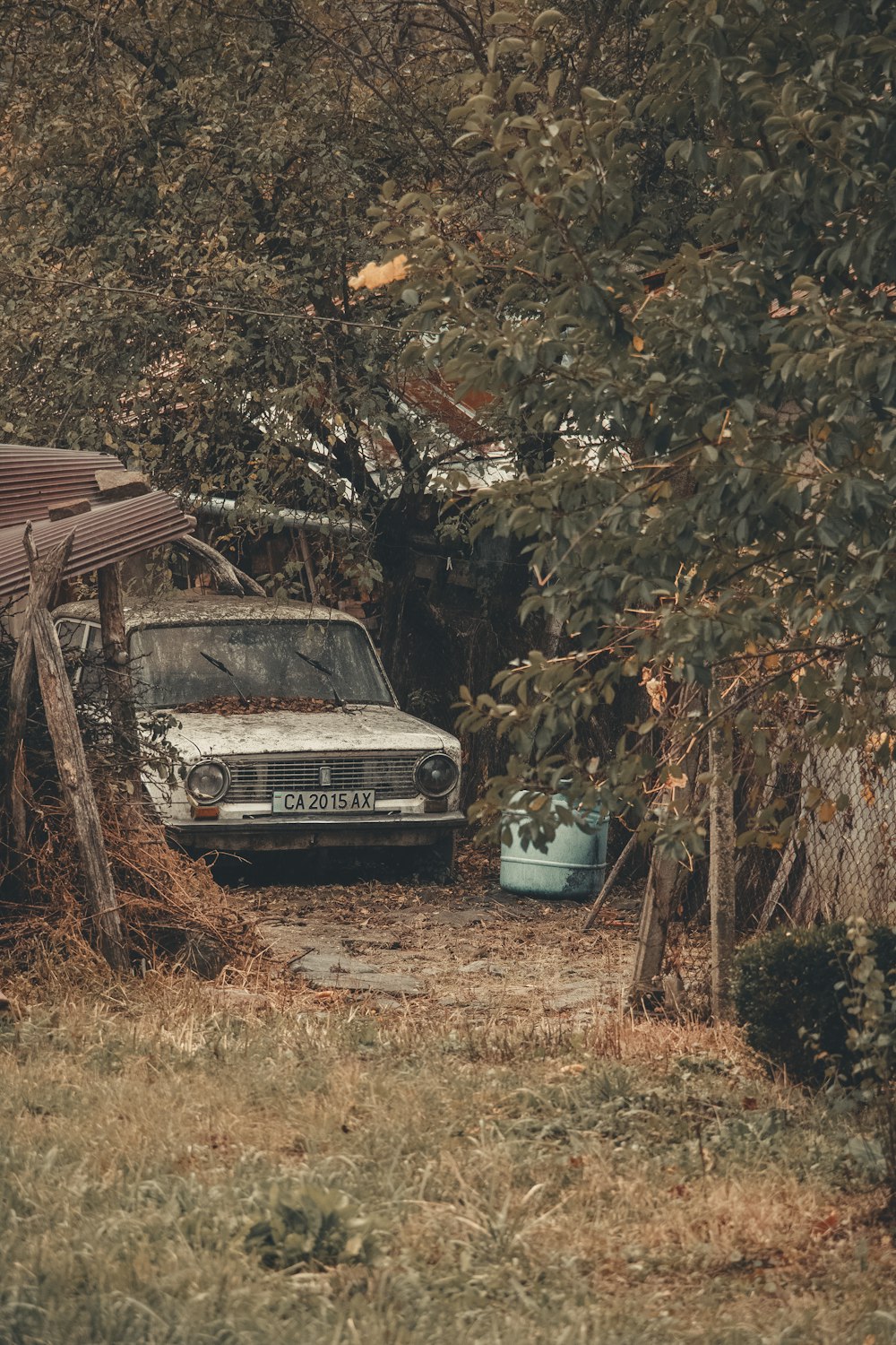 white car parked beside brown wooden house surrounded by trees during daytime