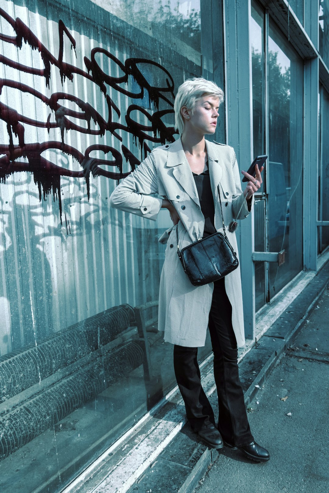 woman in gray coat and black pants standing beside glass wall