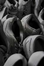 A pile of grey sneakers in varying positions, showcasing textures and details like laces and stitching. The shoes are tightly arranged, giving a sense of abundance.