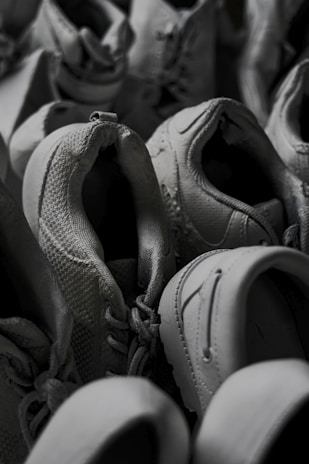 A pile of grey sneakers in varying positions, showcasing textures and details like laces and stitching. The shoes are tightly arranged, giving a sense of abundance.