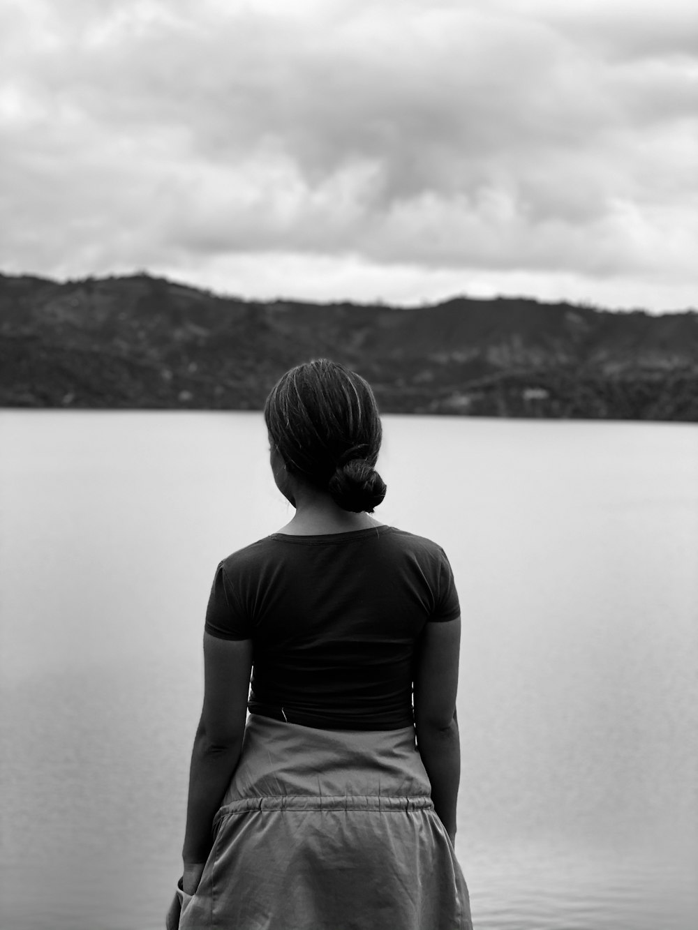 grayscale photo of man in black t-shirt standing near body of water