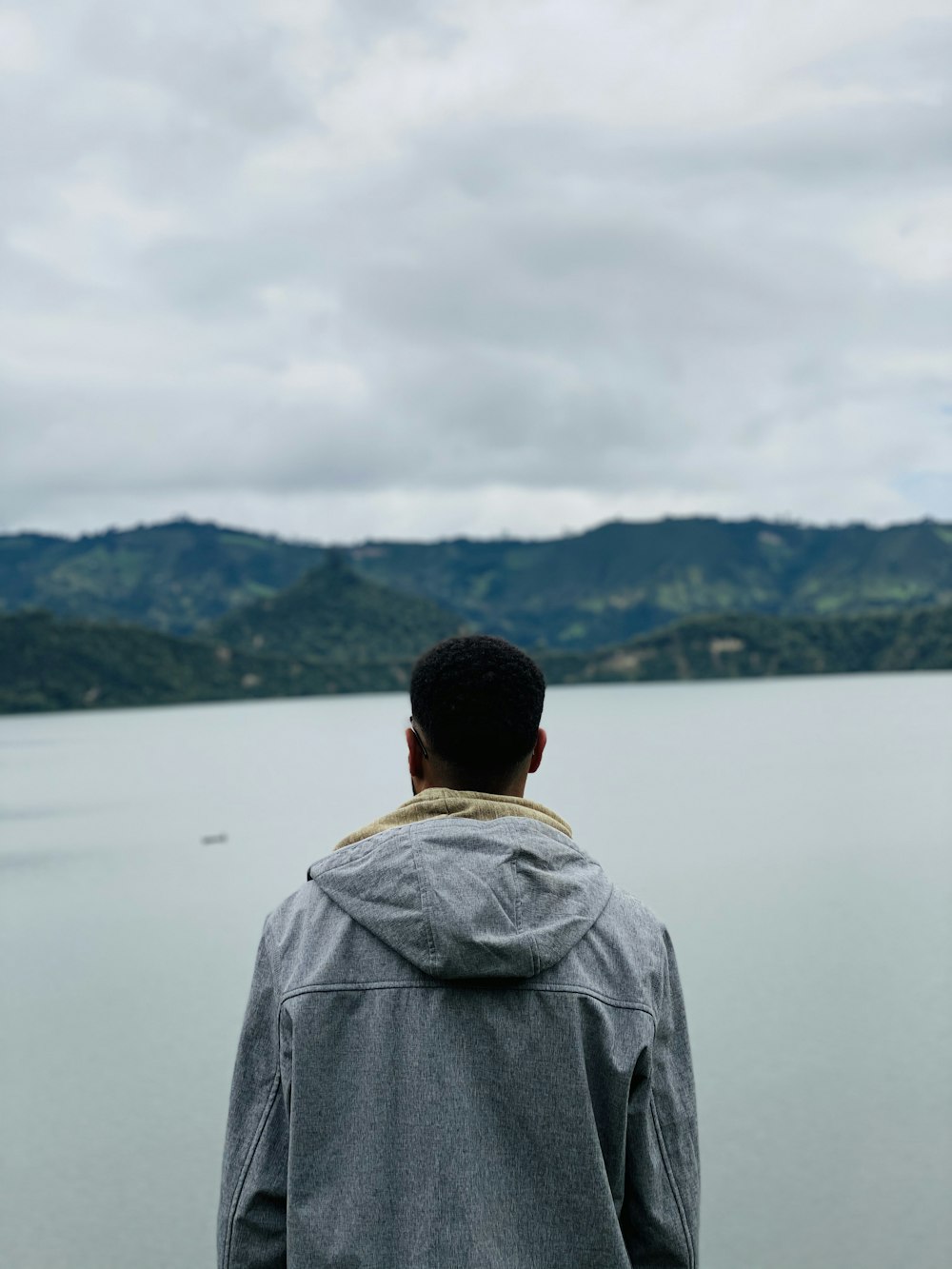 man in grey jacket standing near lake during daytime