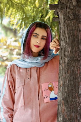 woman in pink button up long sleeve shirt standing beside brown tree