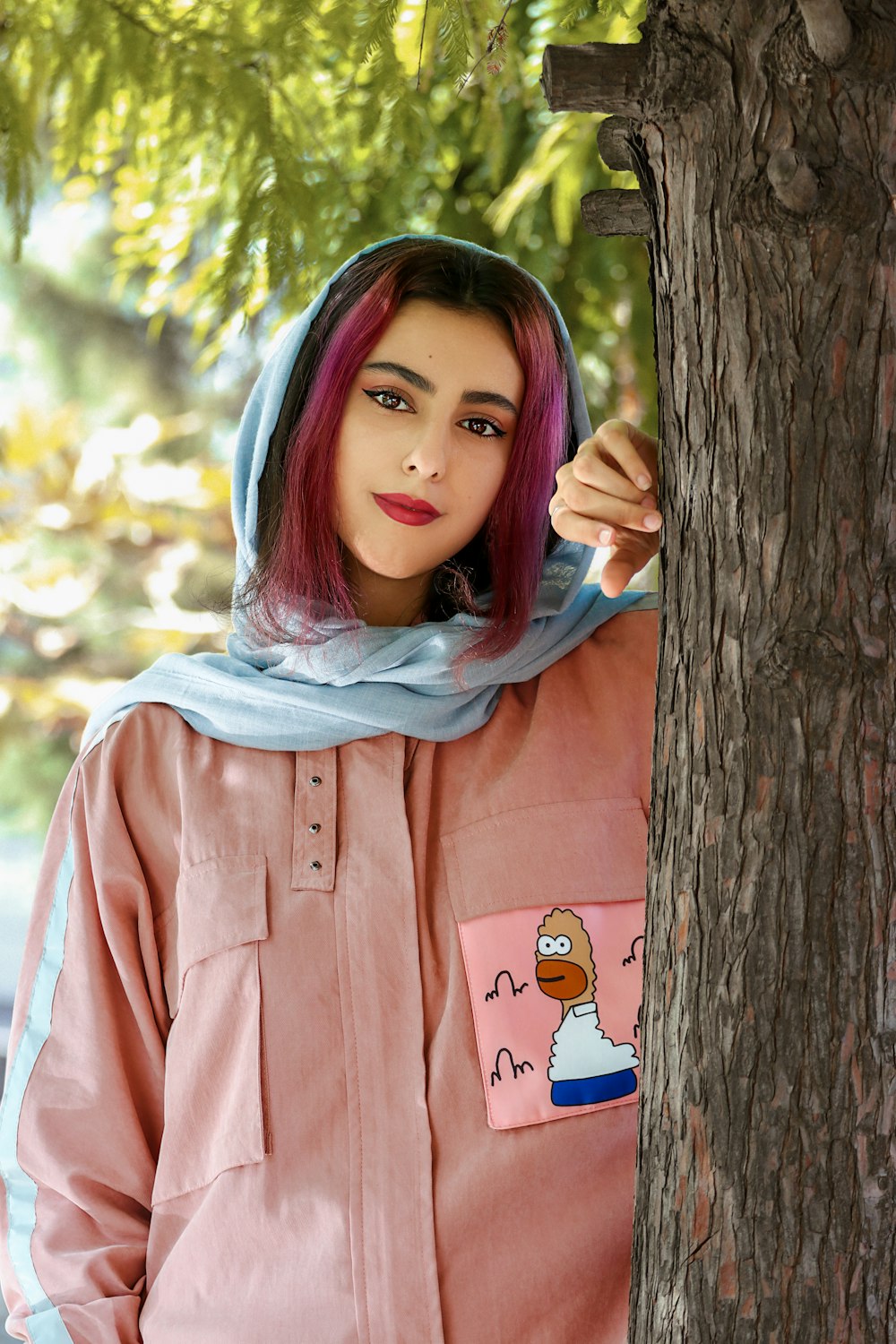 갈색 나무 옆에 서 있는 분홍색 버튼 업 긴팔 셔츠를 입은 여자