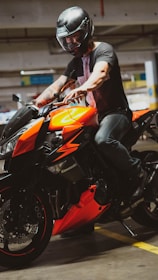 man in black leather jacket riding orange and black sports bike