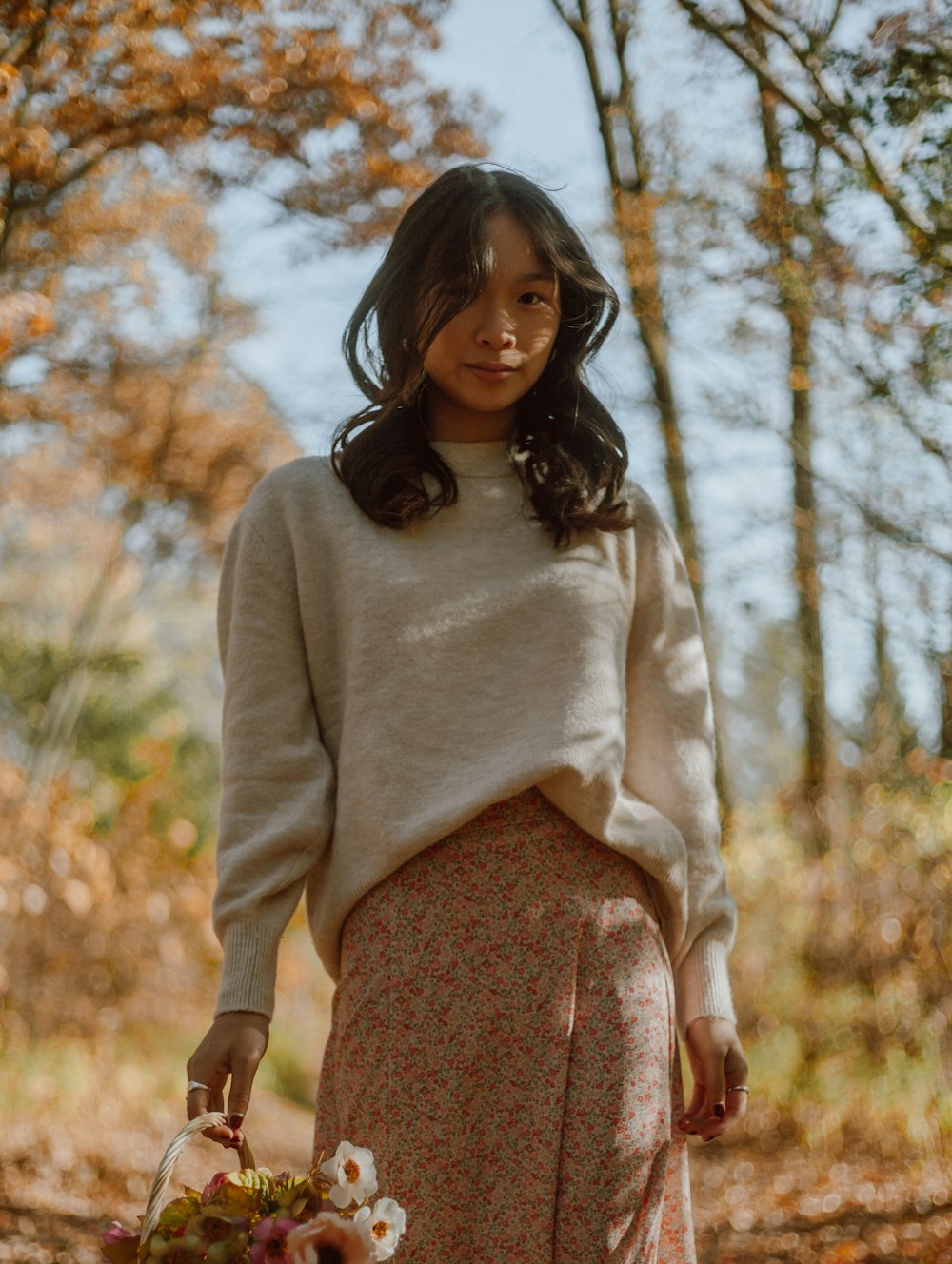 woman in white long sleeve shirt and brown skirt standing near brown trees during daytime