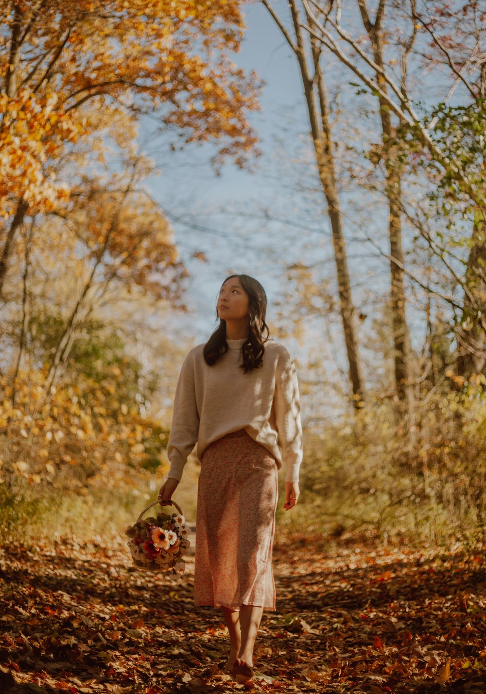 woman in white long sleeve shirt and brown skirt standing on brown dried leaves during daytime