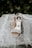 A pair of elegant, open-toed high-heeled shoes adorned with sparkling embellishments rests on a soft lace fabric. The delicate lace features intricate floral patterns, adding a sophisticated touch to the scene. The background consists of green foliage, giving a natural and serene setting.