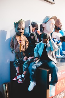 A collection of detailed figurines displayed together. The figures include a humanoid with a wooden texture resembling a tree, another figure wearing a dark hood and camouflage pants, and a figure with a hat and casual clothing. Each figure is posed uniquely, showcasing different attire and accessories.