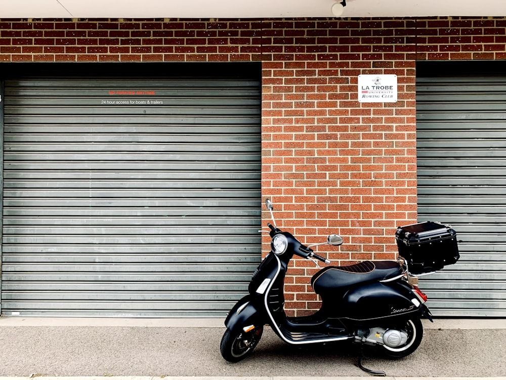 black motor scooter parked beside brown brick wall