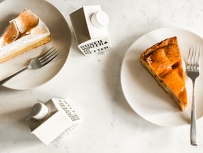 Slices of pie are served on white plates, accompanied by metal forks. Nearby, cartons labeled 'Boxed Water Is Better' are placed on a marble table surface.