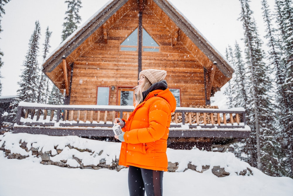 Frau in orangefarbener Jacke steht auf schneebedecktem Boden