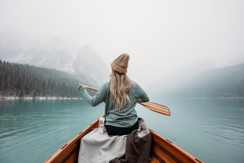 Frau im grauen Langarmhemd sitzt auf braunem Holzboot auf Gewässer während