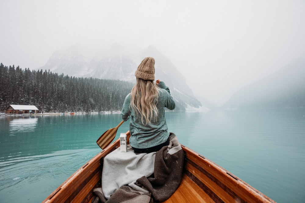 昼間、湖に浮かぶ茶色の木製ボートに座る灰色のパーカーを着た女性