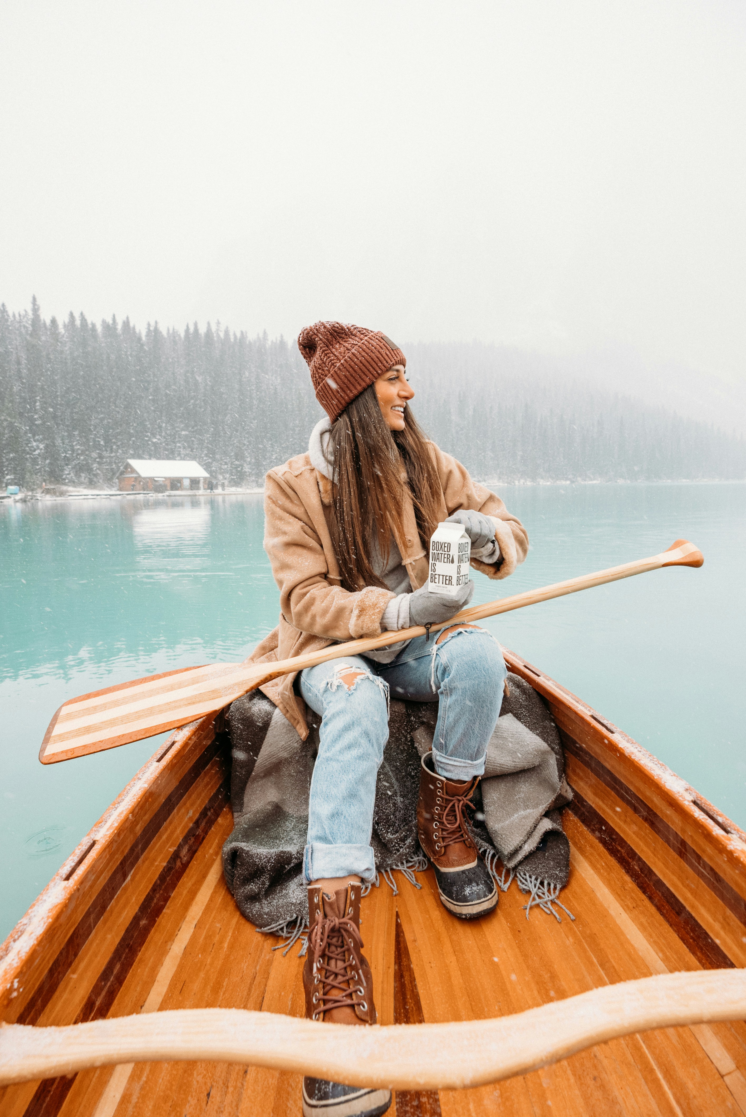 woman in brown jacket and blue denim jeans sitting on brown wooden boat on lake during