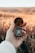 A hand is holding an open brass compass against a blurred natural background, suggesting a field or open landscape. The compass needle points ahead, and the person's sweater is visible, indicating it might be cool weather.