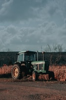 Wide shot of a tractor parked on a dirt path with rolling hills and a cloudy sky background