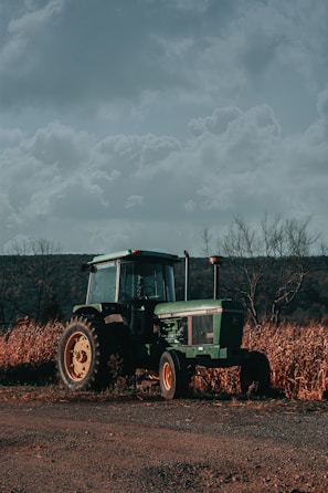 Wide shot of a tractor parked on a dirt path with rolling hills and a cloudy sky background