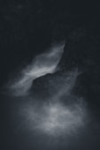 Dark and moody scene of water flowing through rocky surroundings, creating a misty and ethereal atmosphere.