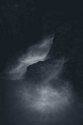 Dark and moody scene of water flowing through rocky surroundings, creating a misty and ethereal atmosphere.
