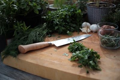 Elegant Damascus kitchen knife resting on a rustic wooden cutting board with fresh herbs.