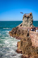 people sitting on brown rock formation near sea during daytime