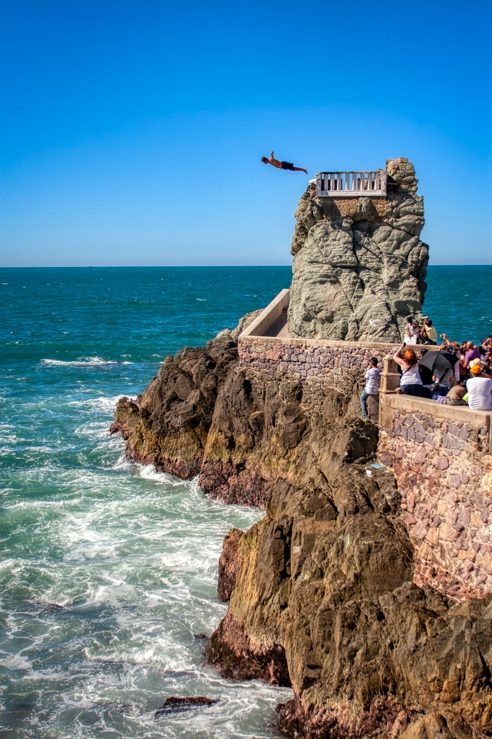 people sitting on brown rock formation near sea during daytime