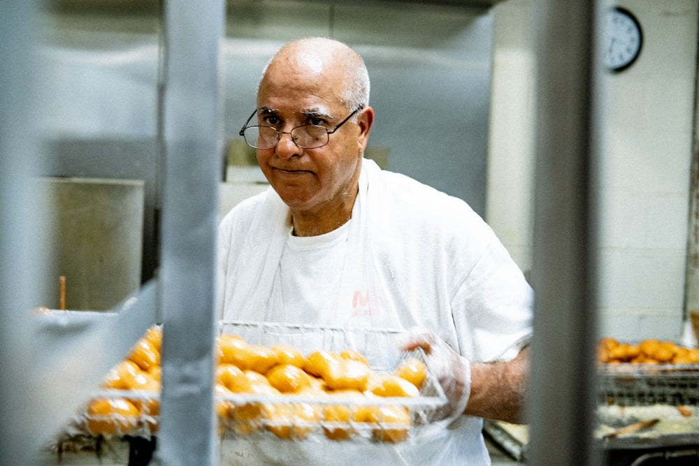 hombre con camiseta blanca de cuello redondo sosteniendo bandeja de frutas naranjas