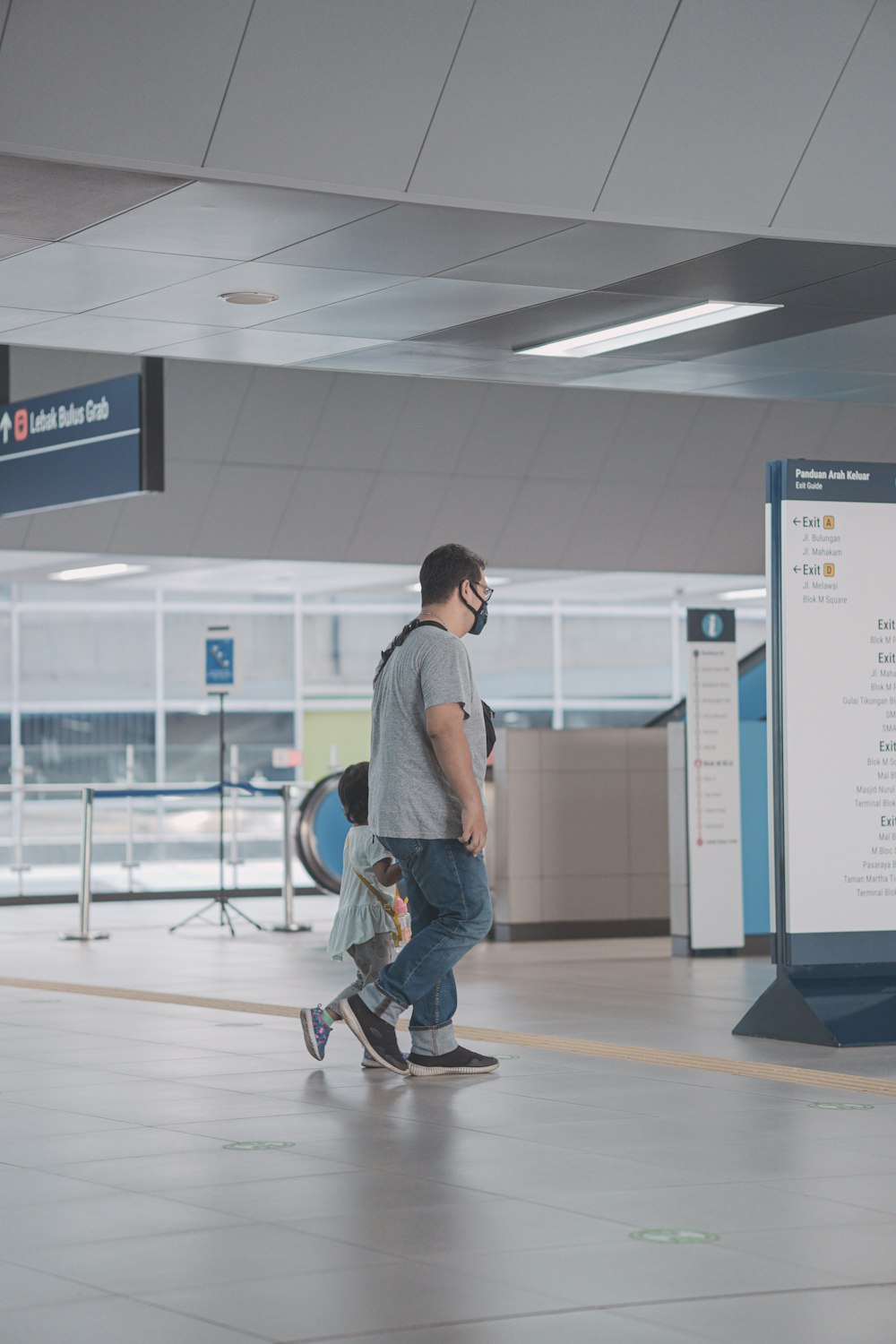 man in gray dress shirt and blue denim jeans standing on white floor tiles