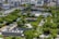 A rooftop garden featuring lush greenery with numerous trees and small glass structures. In the background, a cityscape with modern buildings and a curved structure with vibrant red, yellow, green, and blue panels can be seen.