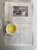 A newspaper is lying open on a table with a cup of light yellow beverage placed on the lower left side of the newspaper. The newspaper's headline reads 'Flexibilität und Kreativität', and it includes a black and white photograph of a vintage car beside a road sign. The text is printed in German.