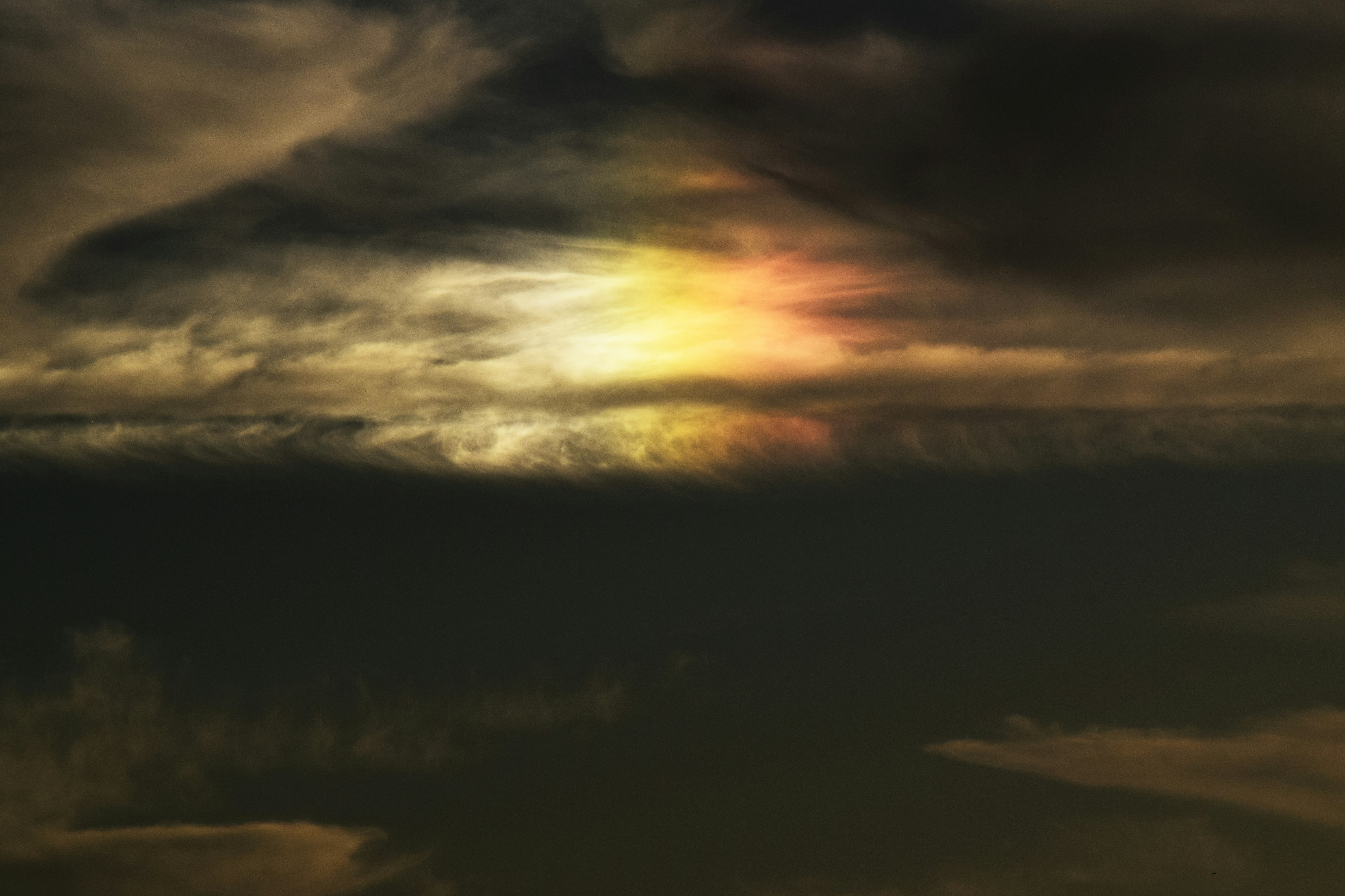 Sun halo and an iridescent patch glow above a dark horizon in a moody dusk sky. This photograph highlights a natural atmospheric phenomenon.