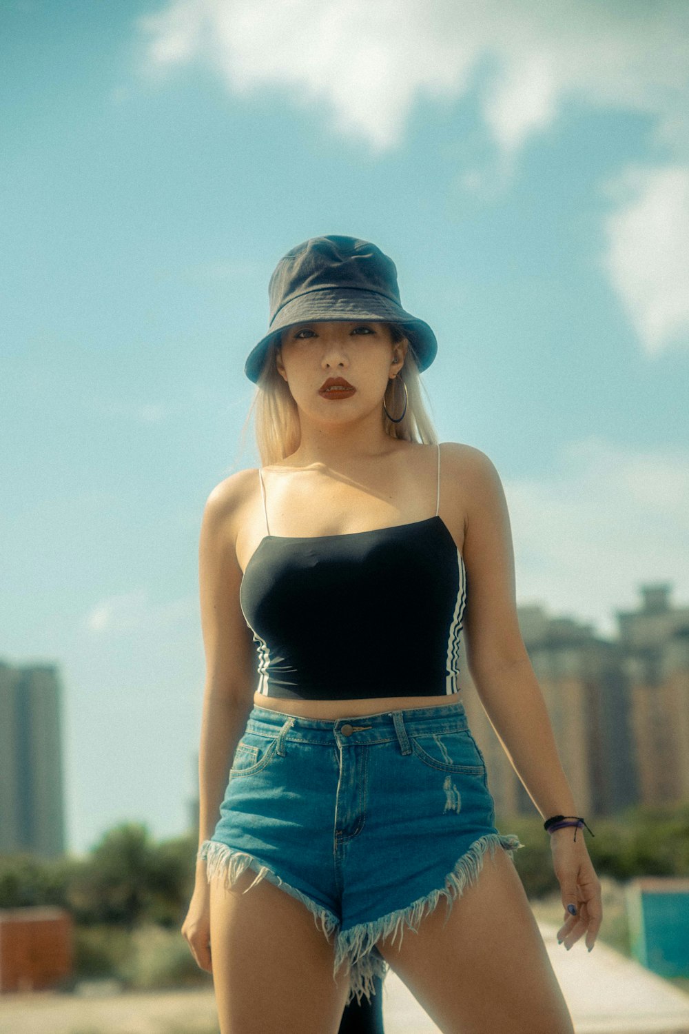 woman in black spaghetti strap top and blue denim shorts wearing blue and white cap